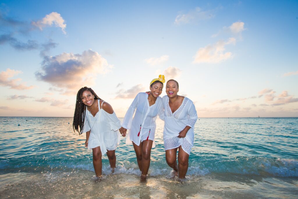 three black women posing for a photo in the water by the sand