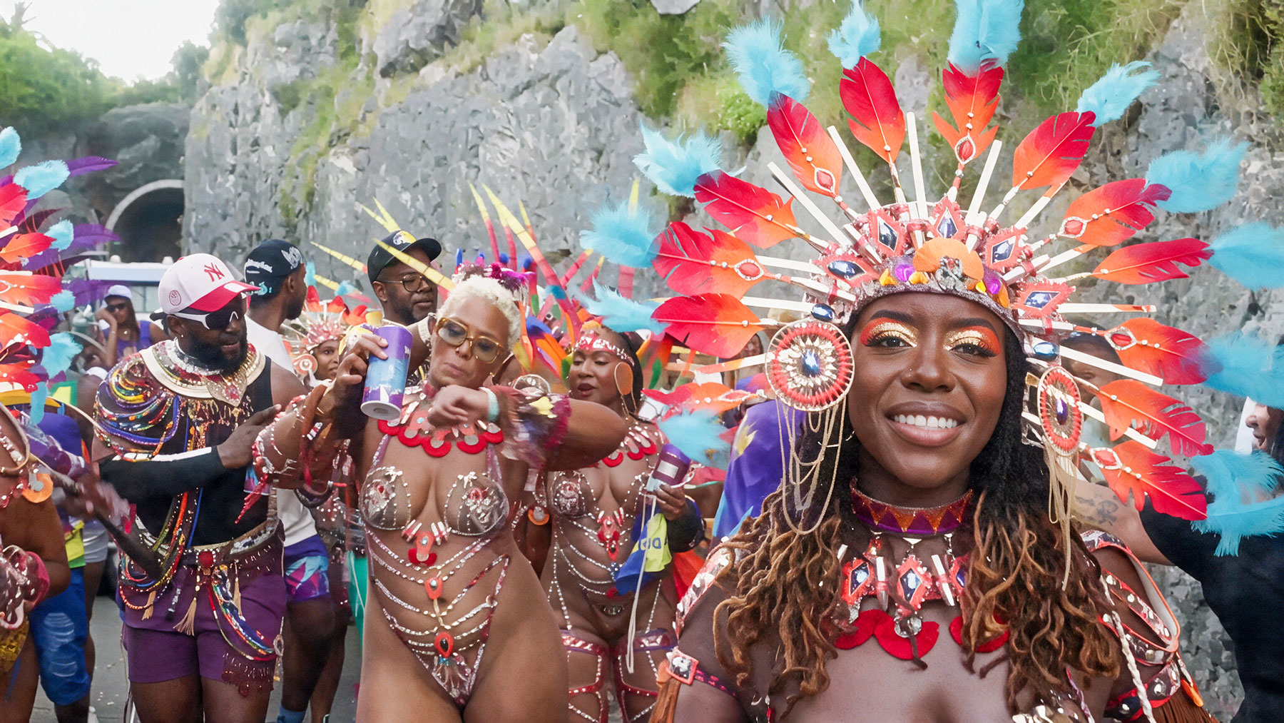 Smiling Carnival reveler in a red and blue feathered headdress with fellow masqueraders